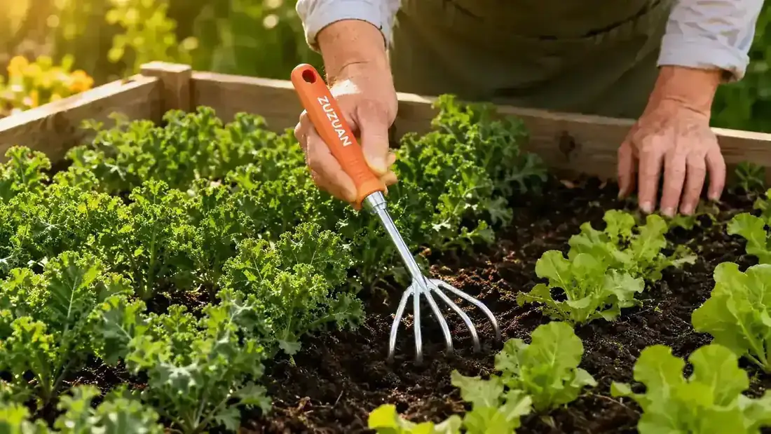 Close-up of the ZUZUAN cultivator tines raking through compacted garden soil with weeds loosening around the tines